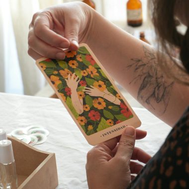 A person holds an 'Intuition' tarot card surrounded by flowers on a table indoors.