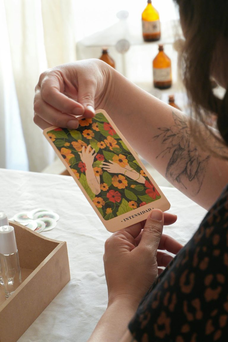 A person holds an 'Intuition' tarot card surrounded by flowers on a table indoors.