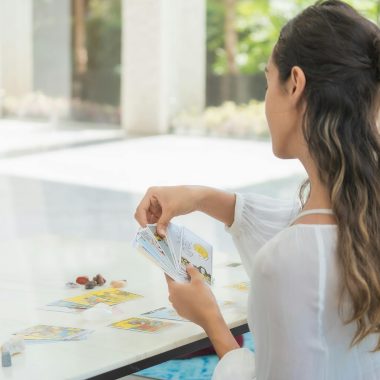 A woman performs a tarot card reading at a well-lit indoor table, focusing on spiritual practice.